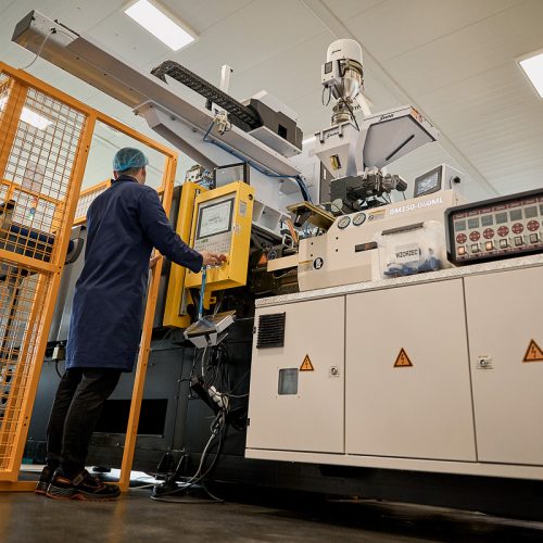 Employé portant une charlotte et une blouse de protection, opérant une machine d’injection dans l’atelier de production.
